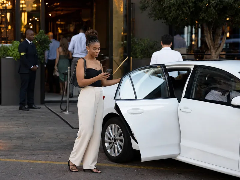 Fictional adult independently checking ride details outside a busy restaurant